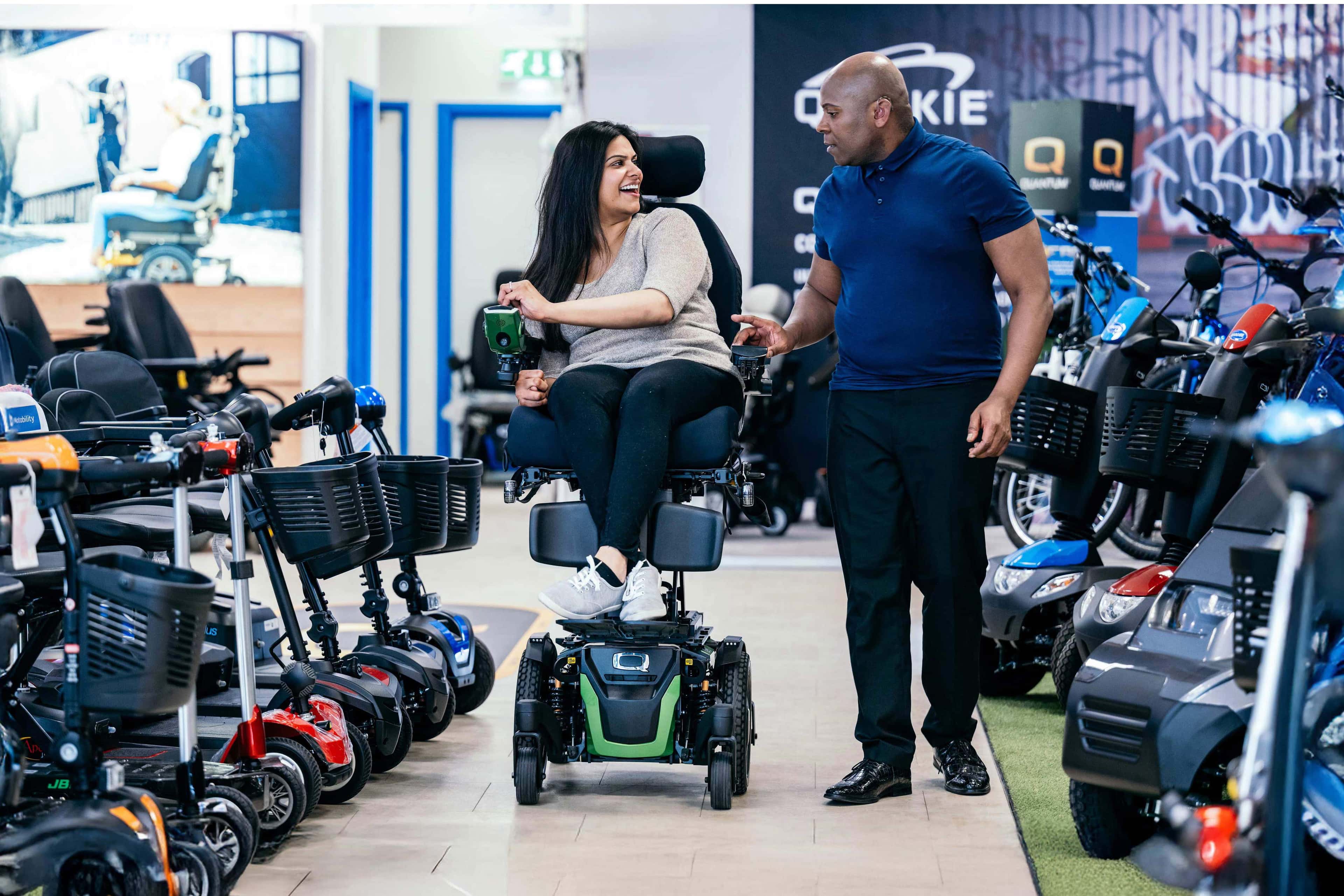 A woman testing mobility scooter, talking to a worker in a dealership